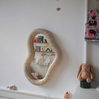Children's room with ecoBirdy Marine Mirror Faded-White and Charlie Chair in strawberry colour way. Decorative mirror with a textured frame in a room with toys and books.
