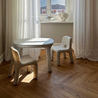 Children's table and chairs set on a wooden floor with light curtains in the background.